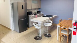 A compact kitchen with a refrigerator, microwave, sink, and a small dining area with stools. - Hollywood Apartments (Yabucoa)