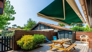 A wooden deck with a picnic table and chairs, a green umbrella, and a small shed.