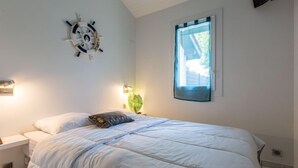A bedroom with a bed, a wall-mounted clock, a window with a view, and a flat-screen TV.