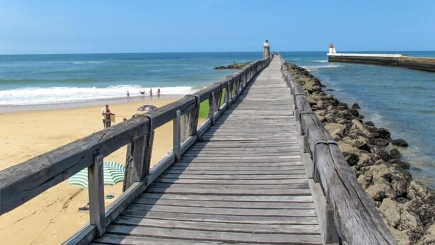 A wooden pier leading to a beach with a lighthouse in the distance.