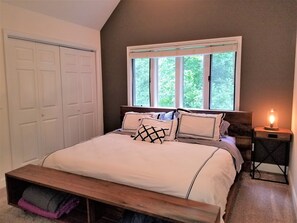 Un dormitorio con una cama, una mesita de noche con lámpara, una ventana con persianas y un armario.