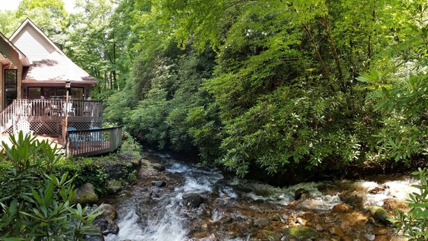 A cabin with a deck overlooking a waterfall, surrounded by dense forest.