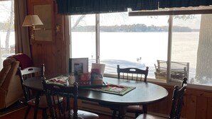 A wooden interior with a round dining table, four chairs, a ceiling fan, and a view of a lake through large windows. - FALL DATES OPEN! Lakeside Cabin - Sandy Beach & Amazing Lake View! (Hillman)
