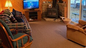 A cozy cabin interior with a wooden ceiling, a fireplace, a television, and a large window overlooking a lake. - FALL DATES OPEN! Lakeside Cabin - Sandy Beach & Amazing Lake View! (Hillman)