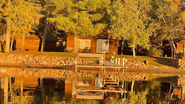 A lakeside cabin with a dock extending into the water, surrounded by trees and a stone wall. - FALL DATES OPEN! Lakeside Cabin - Sandy Beach & Amazing Lake View! (Hillman)