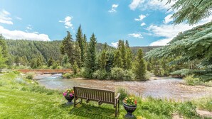 A bench with potted plants, a river, and a bridge in a forested area. - Snowdance 203c by Summit County Mountain Retreats (Keystone)