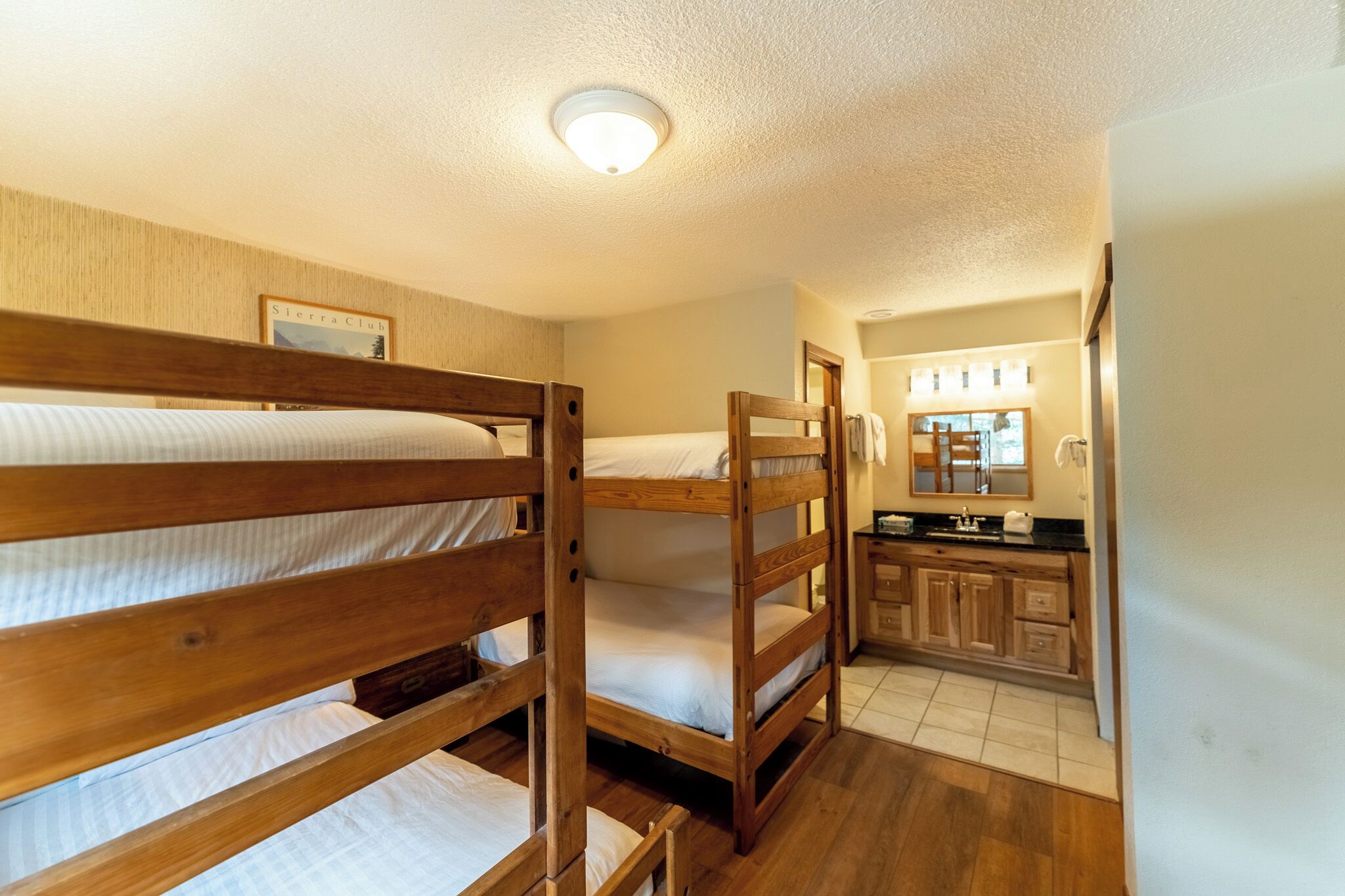 A bunk bed room with a wooden headboard, a small kitchenette with a sink and mirror, and a framed picture on the wall.