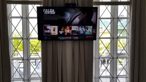 Et hotelværelse med et stort vindue, gardiner og et fladskærms-tv, der viser Netflix.