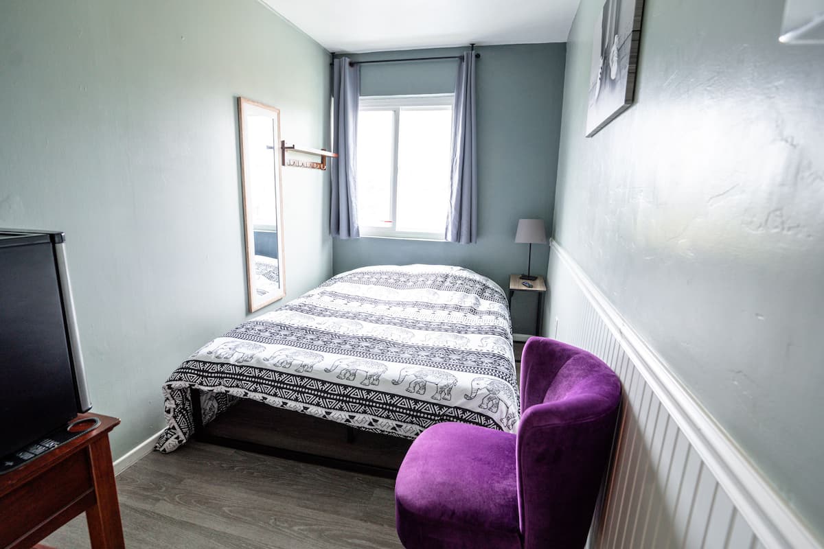 Une chambre à coucher avec un lit, une chaise, une télévision, une fenêtre et une lampe.