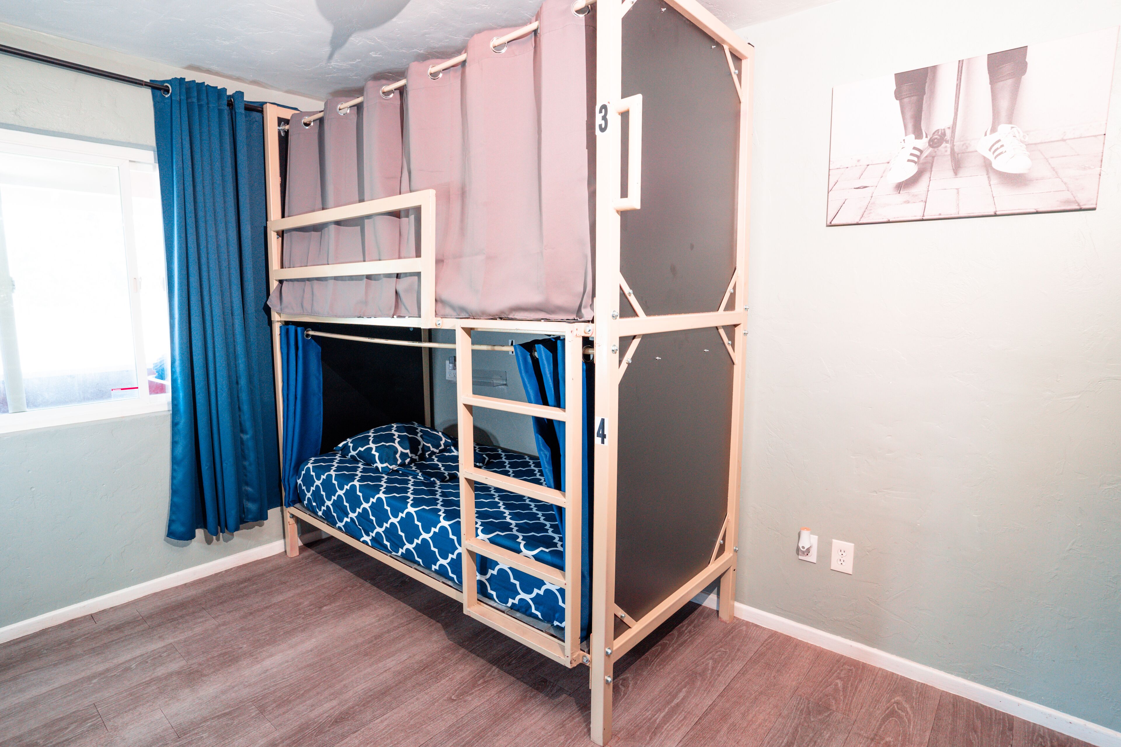 Quarto com beliche, janela, cortinas e um número fixado na parede.