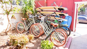 Bicicletas y tablas de surf aparcadas frente a un edificio con puerta roja.