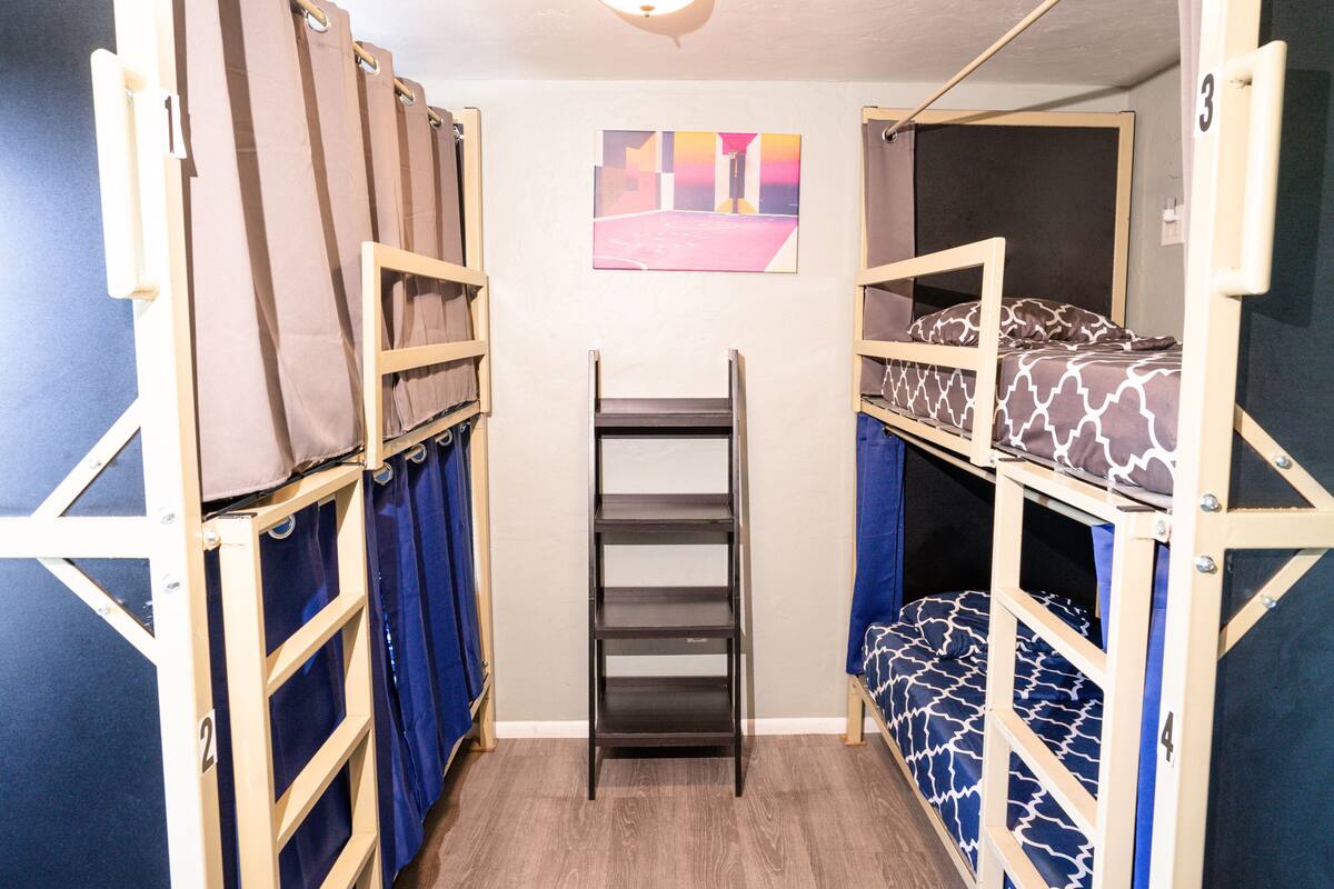 Une chambre de dortoir avec des lits superposés, une étagère centrale et un tableau accroché au mur.