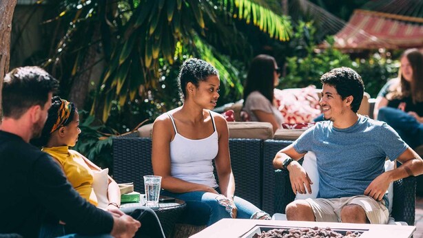 Un grupo de personas sentadas al aire libre en una mesa, con una bebida y un libro.