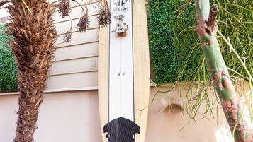 A surfboard leaning against a wall, a wooden bench, and a palm tree.