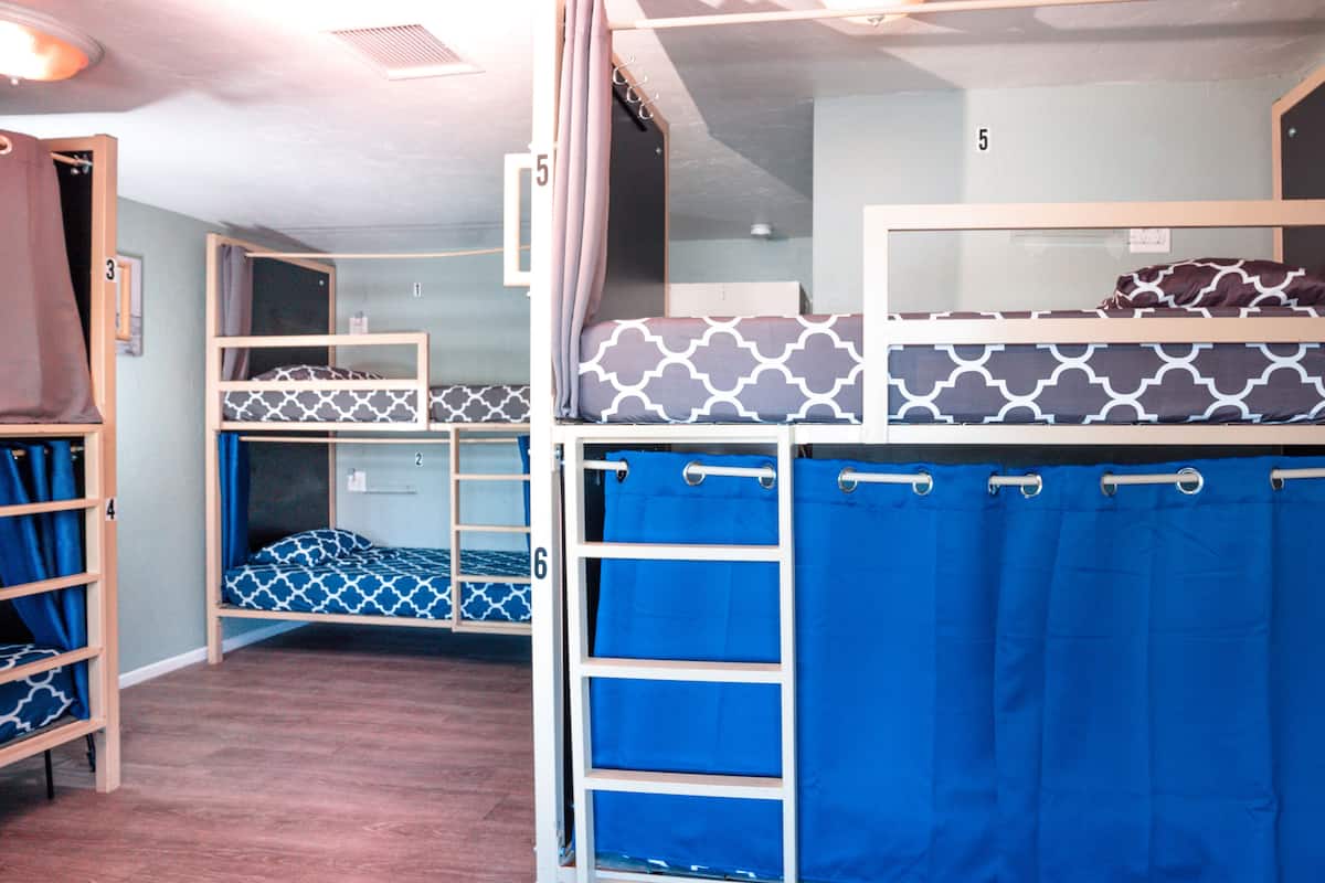 Une chambre de dortoir avec des lits superposés, numérotés de 1 à 6, et un rideau bleu sur le lit du bas.