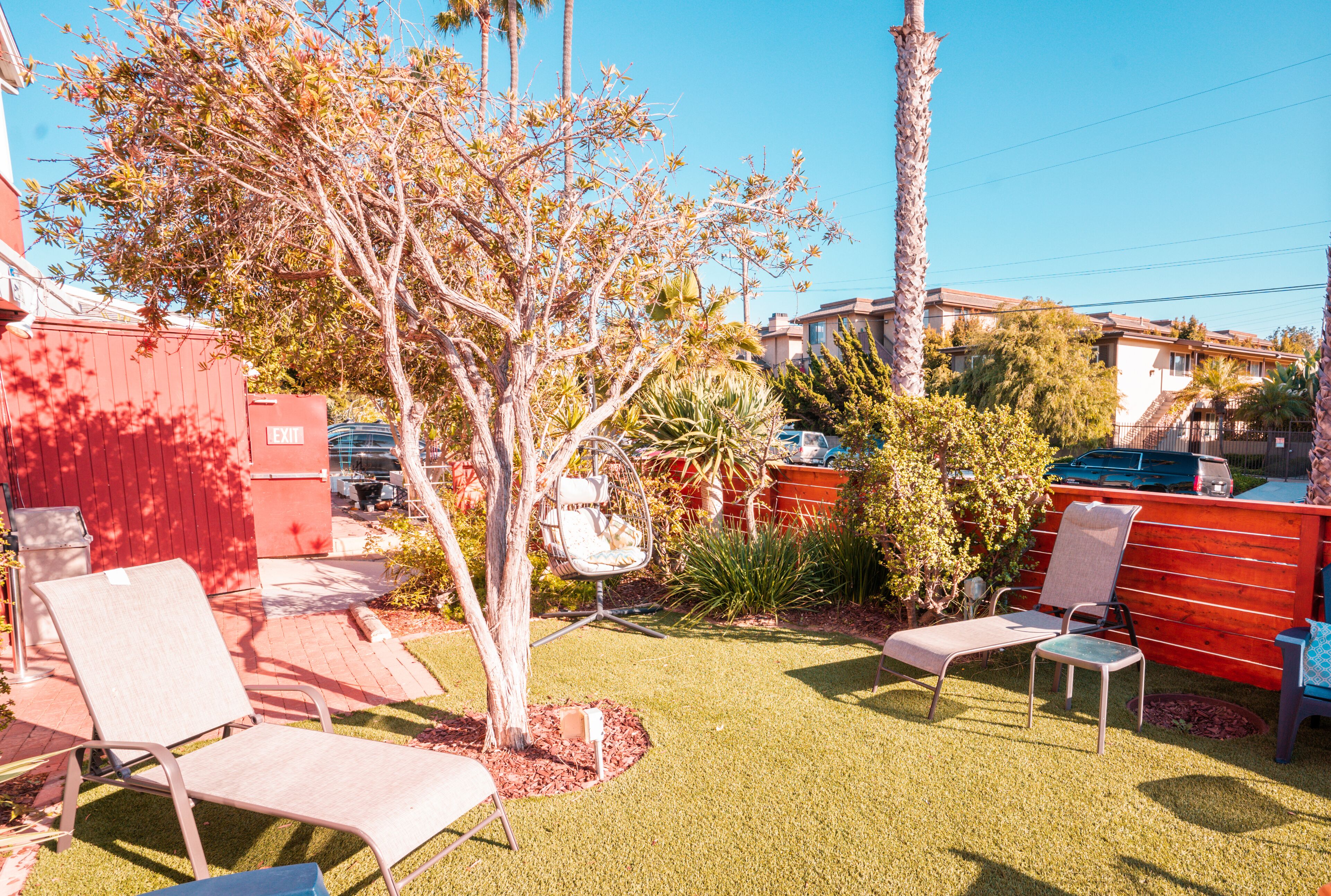 Un jardin avec une pelouse, deux chaises longues, un petit arbre et une clôture rouge.