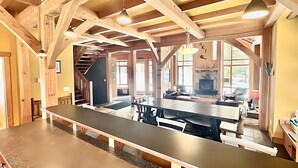 A spacious dining area with a long table and benches, wooden beams on the ceiling, and a fireplace in the background. - Large Ski-In / Ski-Out Timber Frame House, Open Concept, New Hot Tub! (Golden)