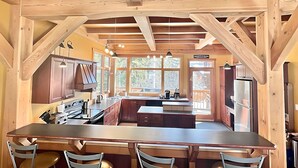 A modern kitchen with wooden beams, a central island, and bar stools. - Large Ski-In / Ski-Out Timber Frame House, Open Concept, New Hot Tub! (Golden)