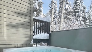 A hot tub with a clear blue interior, surrounded by a wooden deck and snow-covered trees in the background. - Large Ski-In / Ski-Out Timber Frame House, Open Concept, New Hot Tub! (Golden)