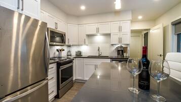 A modern kitchen with stainless steel appliances, white cabinetry, and a central island with wine glasses and a bottle.