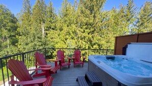 Eine Holzterrasse mit roten Adirondack-Stühlen und einem Whirlpool.
