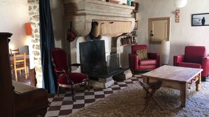 Ein gemütliches Wohnzimmer mit Schachbrettmuster-Boden, Kamin, roten Sesseln und einem Holztisch.