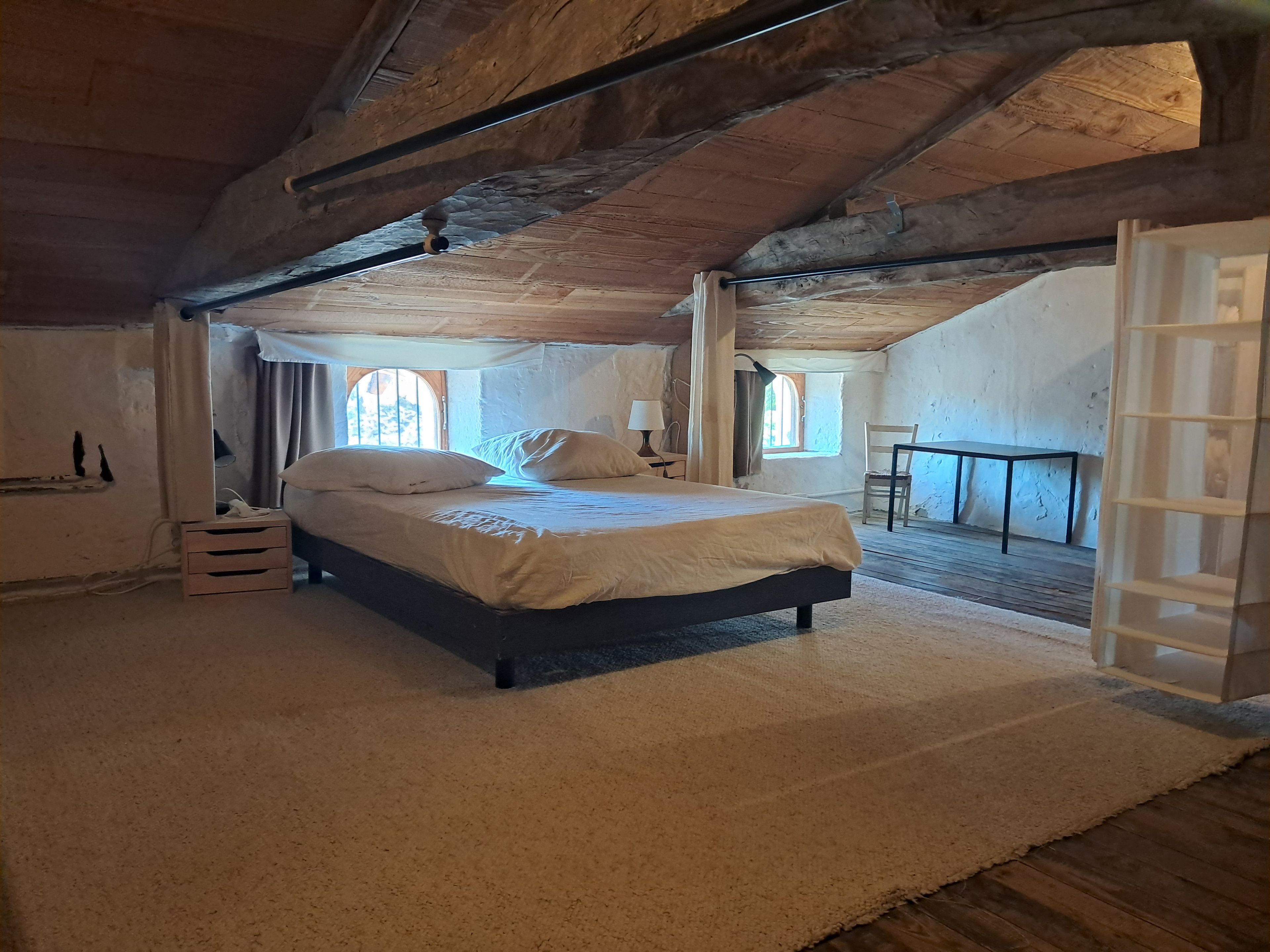 Un dormitorio con cama, piso de madera, ventana y puerta.