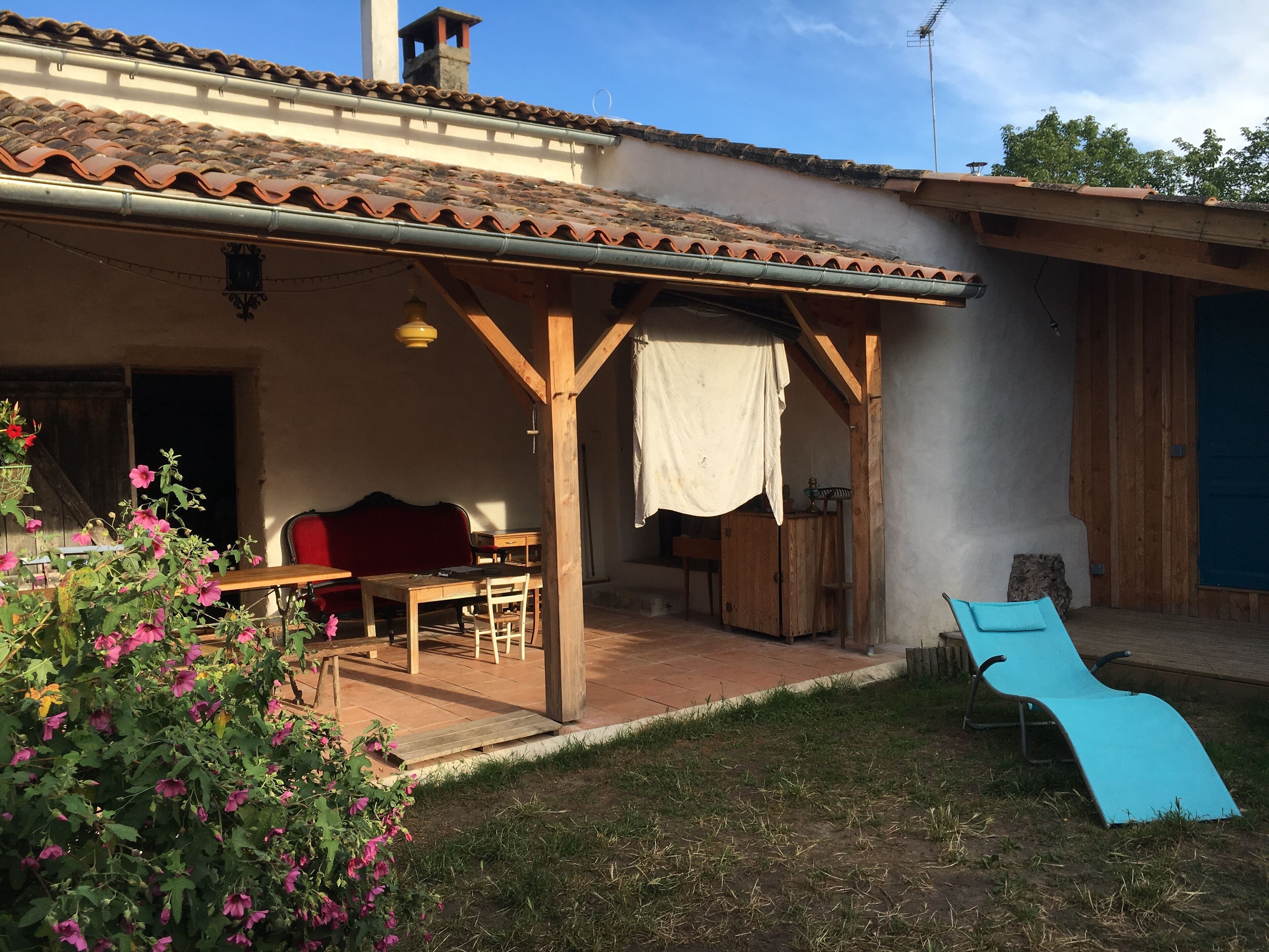 Un'area patio coperta con tavolo e sedie in legno, un divano rosso e una poltrona blu.