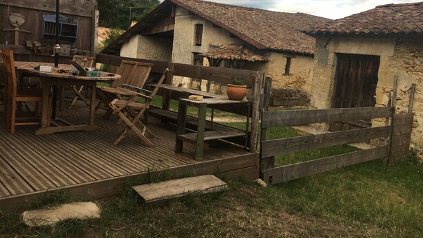 Ein rustikaler Essbereich im Freien mit einer Holzterrasse, einem Tisch mit Stühlen und einem großen roten Sonnenschirm.