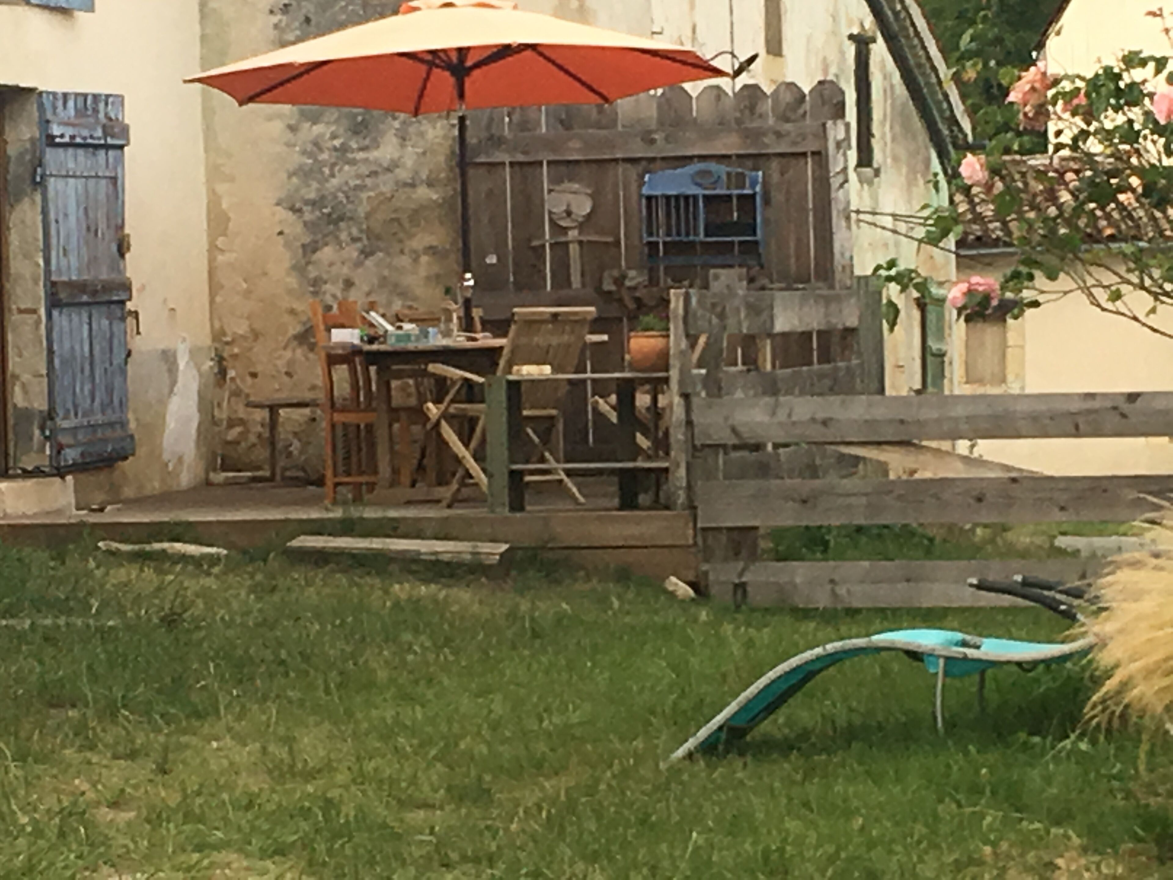 Un espace extérieur aménagé dans un style rustique, avec une table et des chaises en bois, un parasol rouge et une clôture en bois.