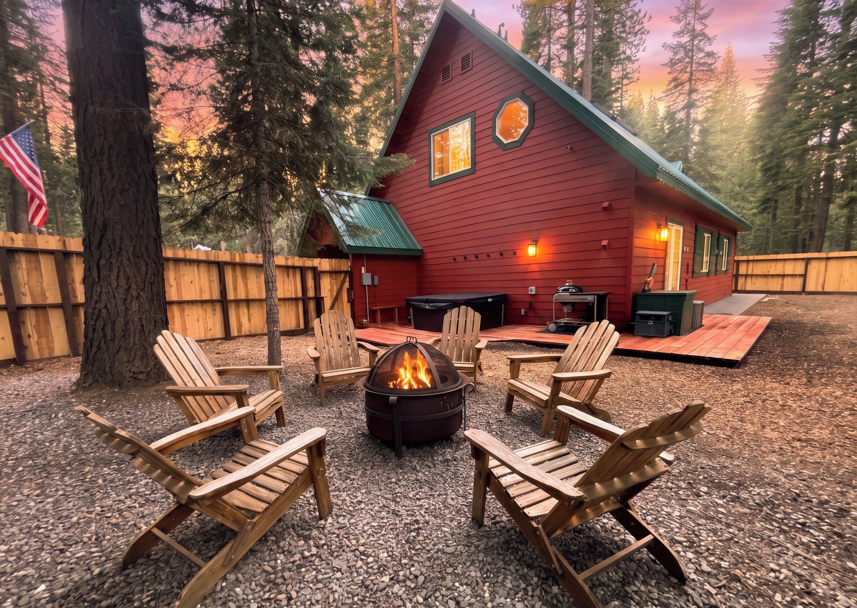A red cabin with a fire pit and Adirondack chairs in a forest setting.