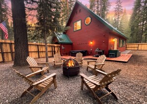 Eine rote Holzhütte mit Feuerstelle und Adirondack-Stühlen inmitten eines Waldes.