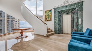 Un interior espacioso con una escalera curva, un sofá azul y un cuadro en la pared.