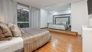 Un dormitorio moderno con una cama grande, un sofá y una zona de estar separada con un banco acolchado.