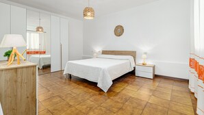 A bedroom with a bed, bedside tables, a dresser, a mirror, and a hanging light fixture.