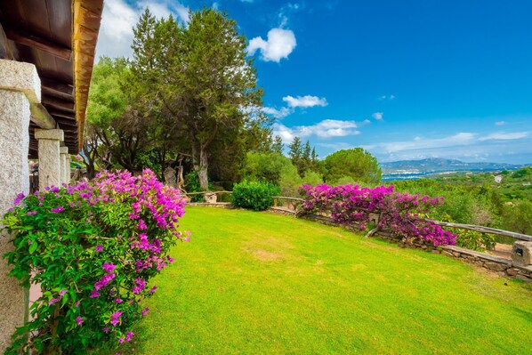 A lush garden with a stone wall, a wooden pergola, and a view of distant hills.