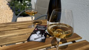 Two wine glasses on a wooden table with a bottle of wine and a menu. - Chambre D'hôtes sur Domaine Viticole Proche Colmar Eguisheim sur Route des Vins (GUEBERSCHWIHR)