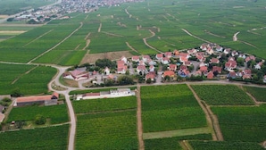 An aerial view of a rural village with neatly arranged agricultural fields and a cluster of houses with red roofs. - Chambre D'hôtes sur Domaine Viticole Proche Colmar Eguisheim sur Route des Vins (GUEBERSCHWIHR)