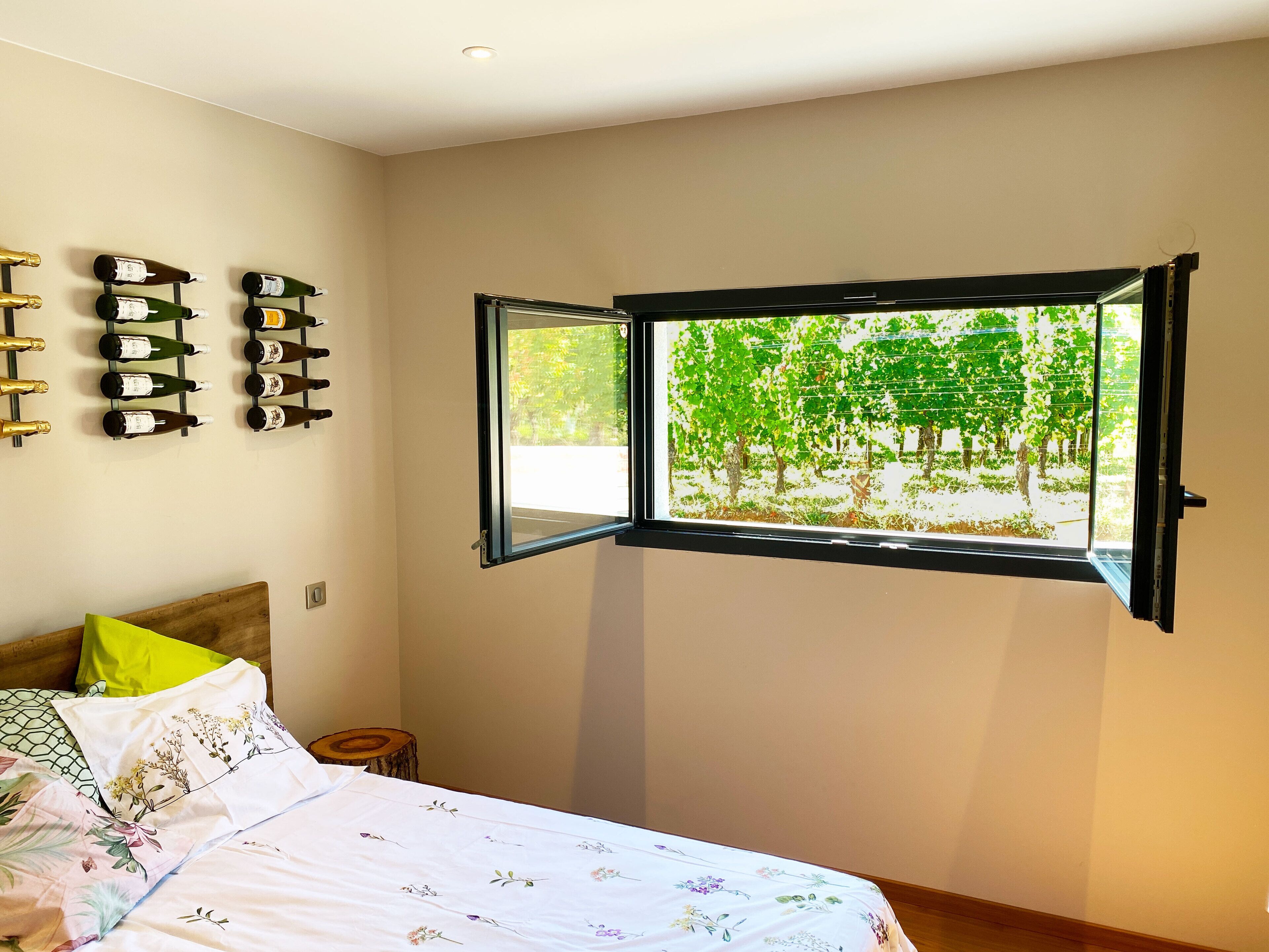 Un dormitorio con cama, ventana que ofrece vista despejada de árboles y una estantería de pared para vinos.