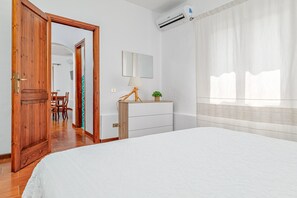 Un dormitorio con una cama, una puerta de madera, un tocador, una lámpara, un espejo y un equipo de aire acondicionado.
