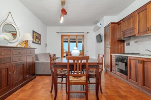 Una cocina con armarios de madera, una mesa de comedor con sillas, un sofá y vistas a través de un ventanal.
