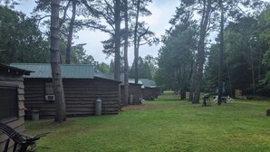 A campground with multiple wooden cabins, a grassy area, and trees. - Moreno's Cottages Cabin #10 -2 Bed/2 Bath Adirondack 4 season Cabin in the pines (Saranac Lake)