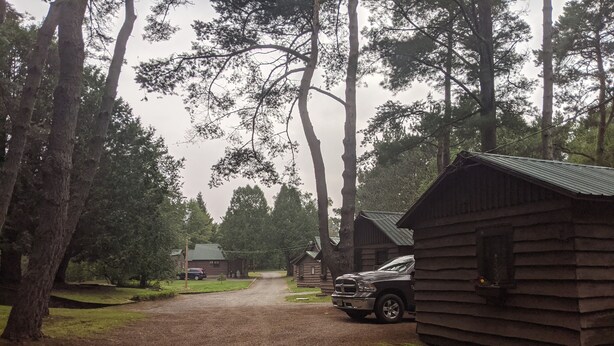 A rustic cabin-style lodging area with a gravel driveway leading to a wooden cabin. - Moreno's Cottages Cabin #10 -2 Bed/2 Bath Adirondack 4 season Cabin in the pines (Saranac Lake)