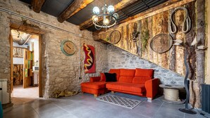 Una habitación con pared de piedra, un sofá rojo, una araña y un rascador para gatos.