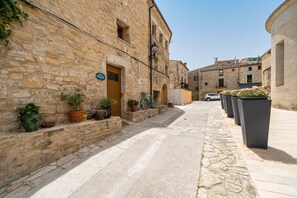 Une ruelle pavée étroite, bordée de bâtiments des deux côtés, avec des plantes en pot et une voiture garée.