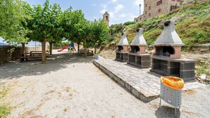 Un área pavimentada con bancos de piedra, un parque infantil y un edificio de piedra con un campanario.