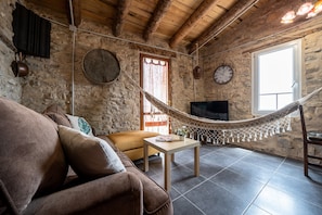 A rustic living room with stone walls, a hammock, a sofa, a television, and a clock.