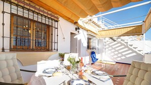 Una mesa de comedor con platos, cubiertos y vasos, una ventana con barrotes y una escalera que lleva a un nivel superior.