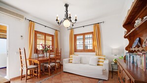 Una habitación con una mesa de comedor, sillas, un sofá, una araña y una estantería.