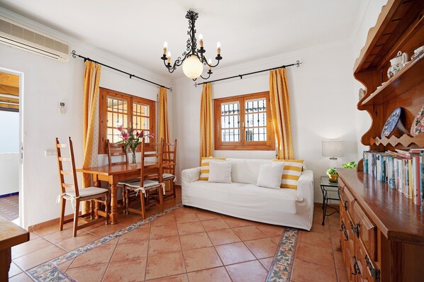 Una habitació amb taula de dinar, cadires, sofà, pèndol i prestatgeria.